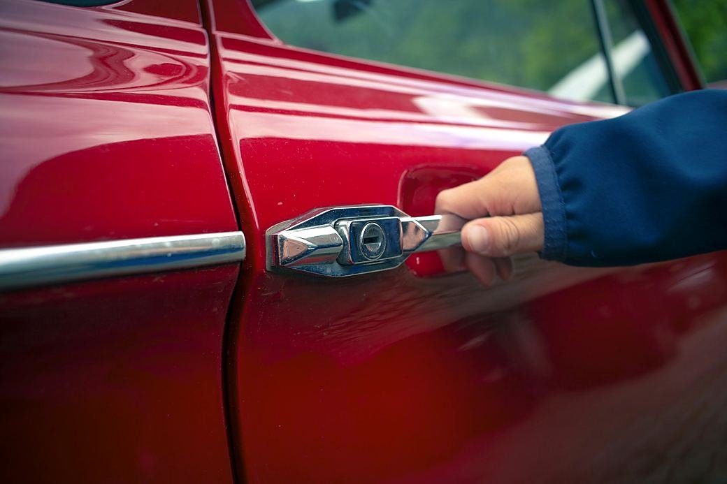A hand pulling the door handle of a locked red car