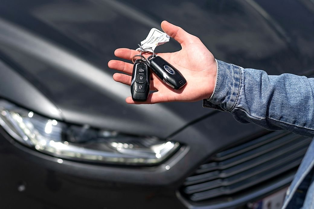 A replacement car key held in a hand beside a car