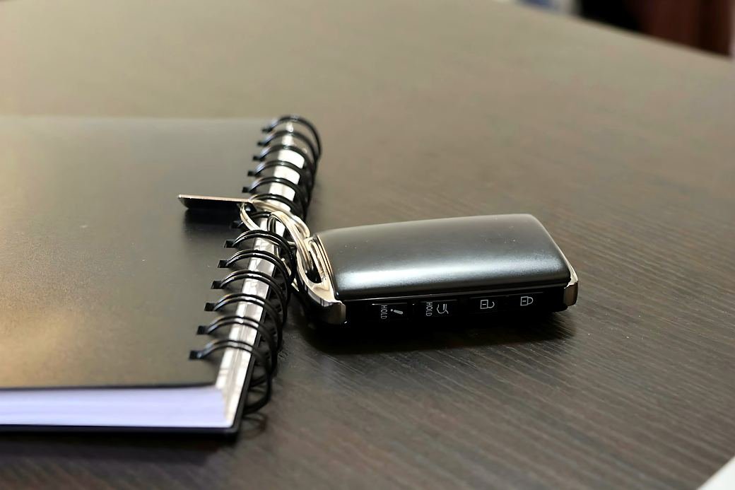 A spare car key lying on a desk next to a notebook